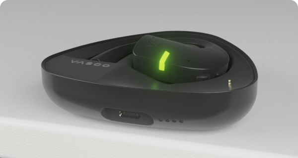 Se coloca un auricular Vasco Translator E1 dentro de su estuche de carga. Los indicadores LED parpadeantes muestran el nivel actual de batería del estuche y del auricular. 