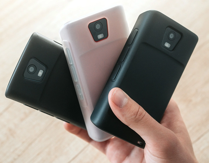 Persona que sostiene tres dispositivos Traductor Q1 en fundas de silicona, mostrando tres colores diferentes de funda: Solid Black, Dark Caramel, and Milky White.