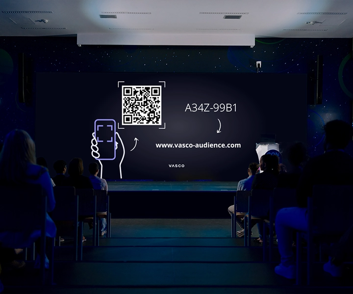 Una gran pantalla situada en la sala de conferencias muestra las instrucciones «Únase a Vasco Audience», con indicaciones para los participantes sobre cómo acceder a la sesión.