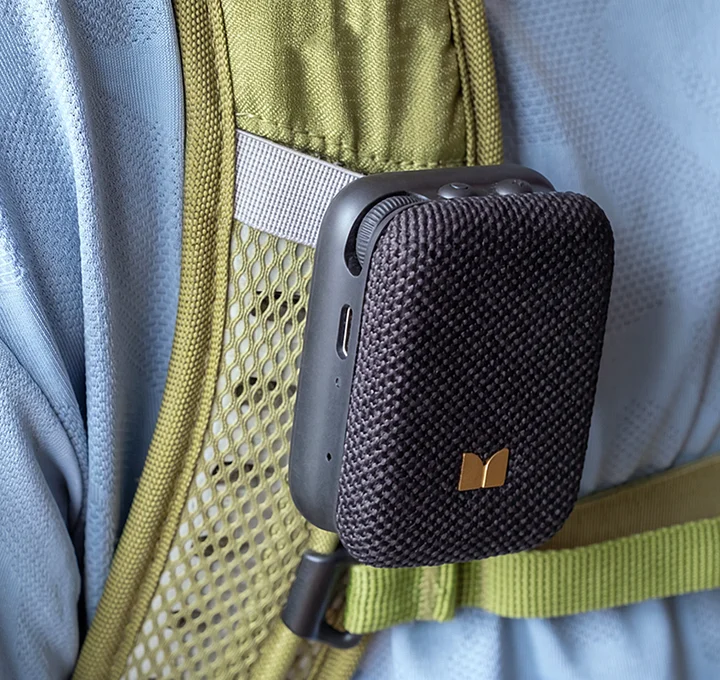 Mini altavoz Bluetooth negro sujeto a la correa verde oliva de una mochila
