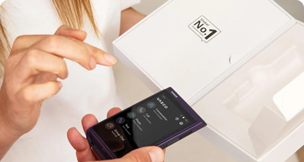 Un primer plano de una persona sacando de su caja blanca de venta al público un Traductor Q1 de color morado.